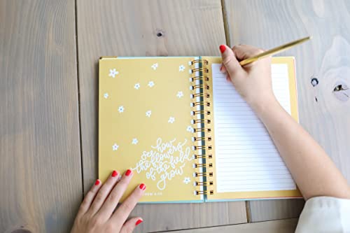 Teen girl writing in spiral-bound Prayer Journal for Teen Girls with yellow floral cover and inspirational quote, using gold pen on wooden table