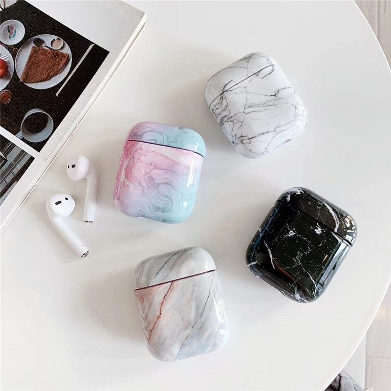 Luxury White Marble AirPods Case collection displayed on a white table with wireless earbuds and assorted marble designs.