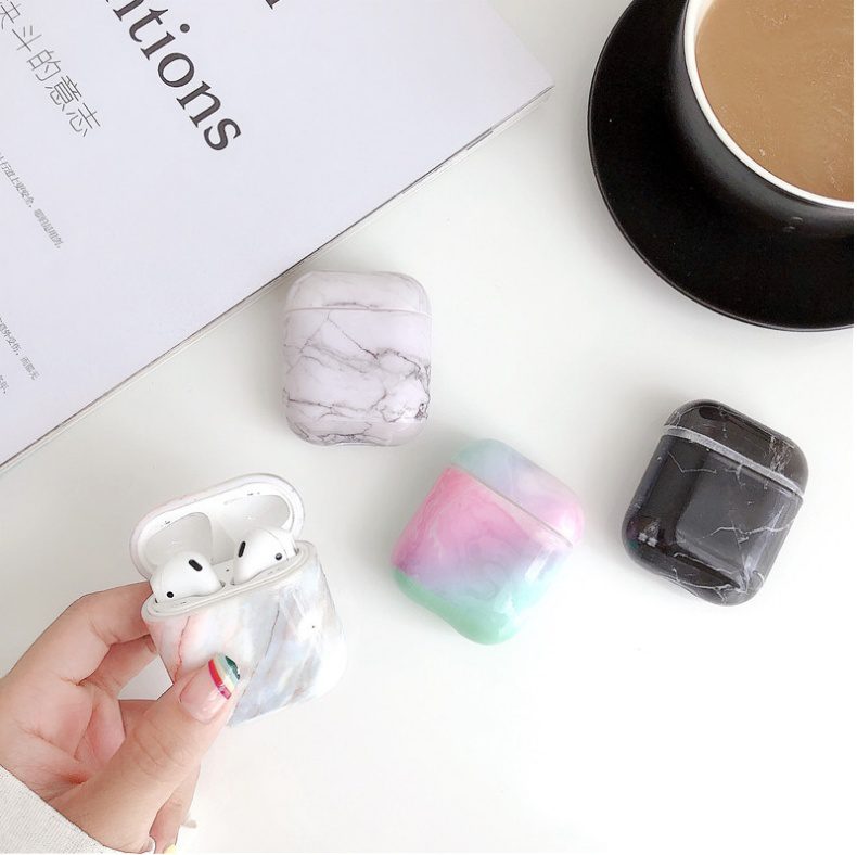 Luxury White Marble AirPods Case held in hand with three additional marble and pastel cases on white surface.