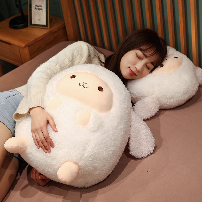 Person lying on bed cuddling two round sheep plushies, one used as a pillow