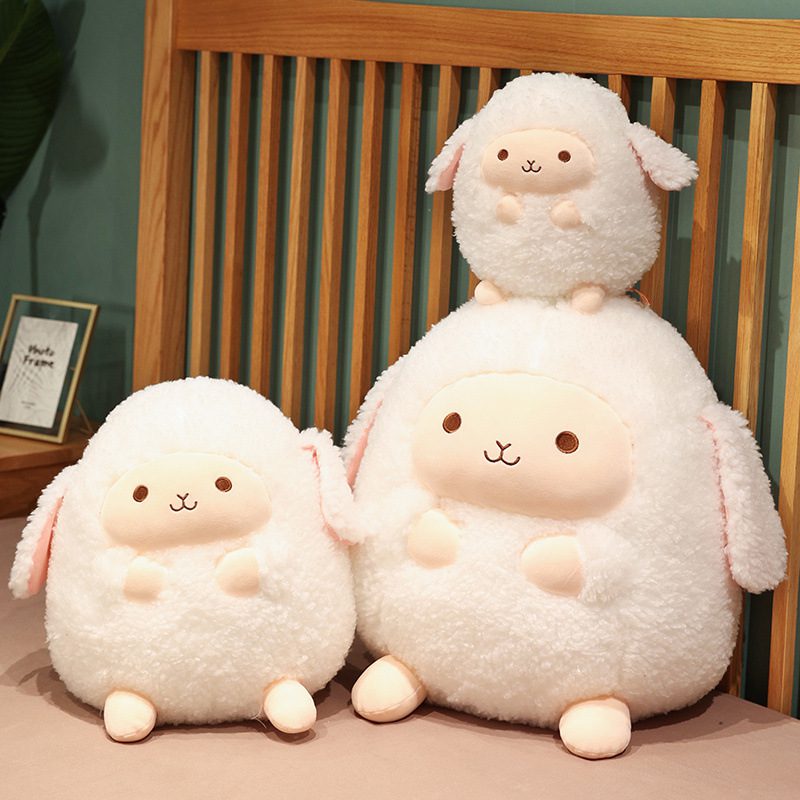 Three round sheep plushies in different sizes arranged on a bed with wooden headboard.