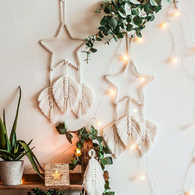 Two star-shaped dream catcher wall decorations with macramé tassels and warm string lights above a decorated shelf.