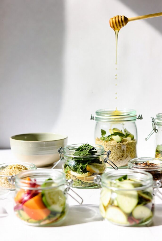 Eczema Healing Foods: What to Eat and Avoid for Better Skin 4 Glass jars filled with fresh vegetables, grains and seeds with honey dipper dripping golden honey, clean minimalist composition